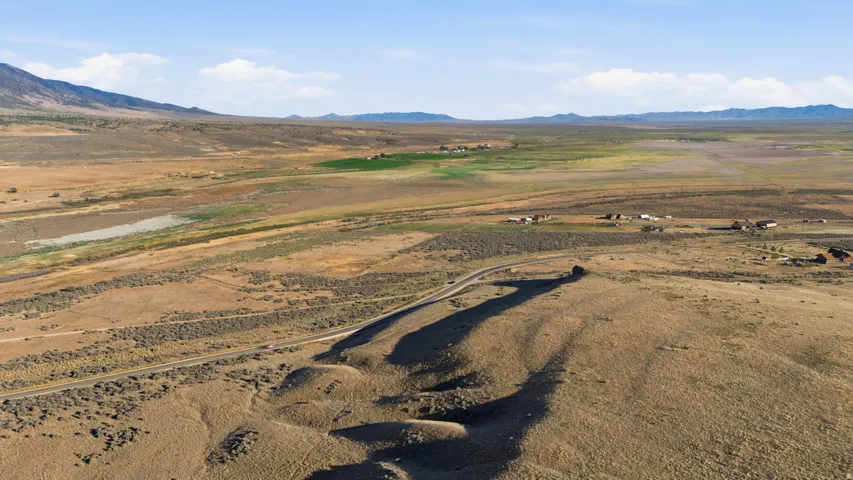 Expansive open land featuring a winding road, distant mountains, and scattered structures