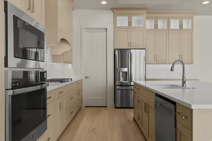 Modern kitchen featuring stainless steel appliances, light-toned cabinetry, wood-finish flooring, a central island with an integrated sink, and white countertops
