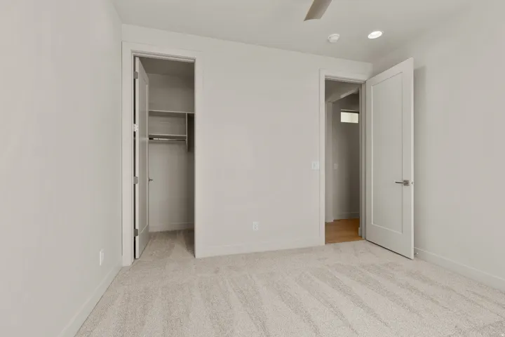 Neutral-toned room featuring light-colored carpeting, two paneled interior doors, and a ceiling-mounted fan