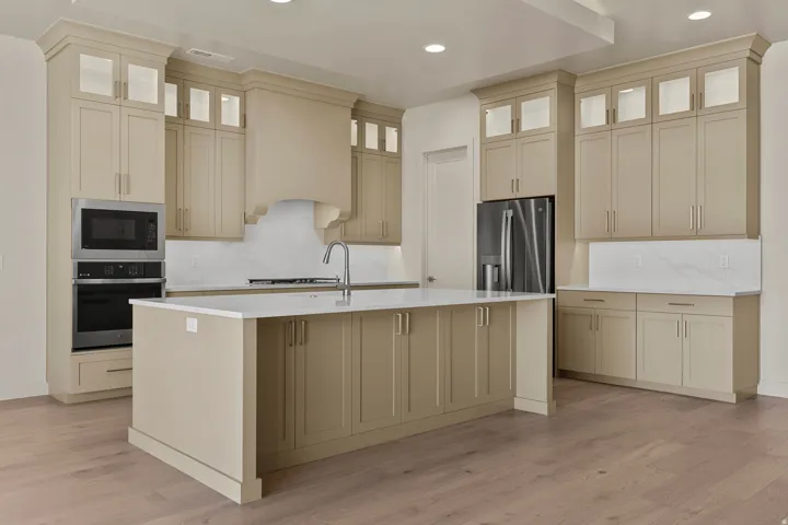 Spacious kitchen featuring an expansive center island with seating, extensive cabinetry with illuminated glass-front uppers, stainless steel appliances, a built-in microwave and oven, and wood-finish flooring