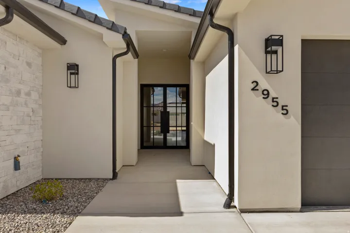 Entryway featuring a modern double-door with black framing, stucco exterior, stacked stone accent wall, decorative exterior lighting, and a paved walkway