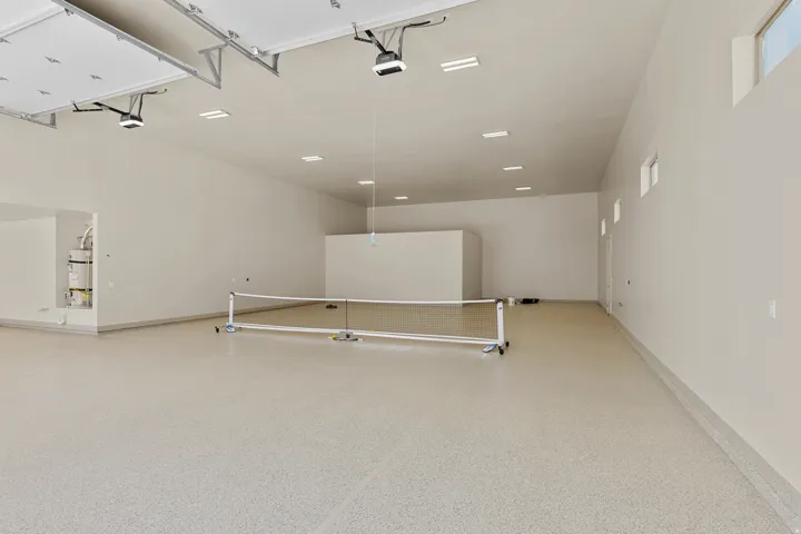 Expansive multi-car garage featuring a light-colored epoxy floor, multiple overhead garage door openers, recessed ceiling lighting, and high-set windows providing ambient illumination
