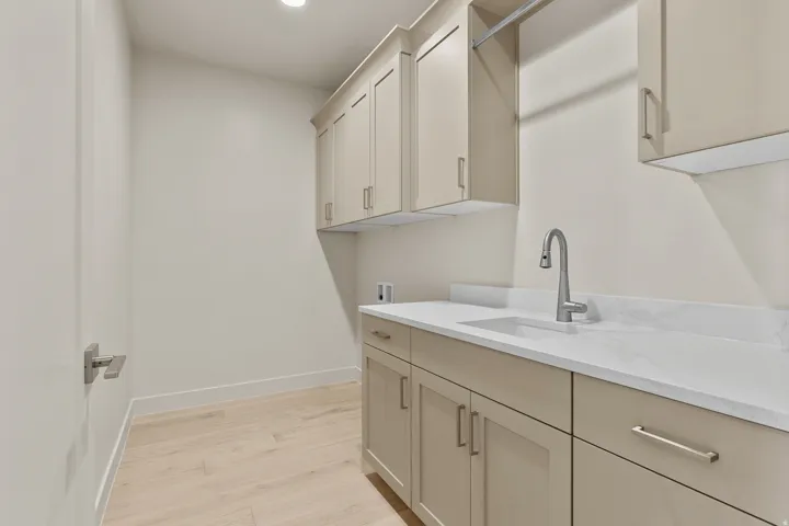 Laundry area featuring light wood-finish flooring, extensive cabinetry with brushed nickel hardware, and a white countertop with an integrated sink and gooseneck faucet