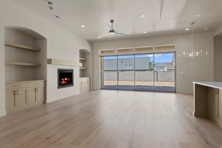 Open-concept living space featuring wood-finish flooring, a contemporary fireplace with mantel, built-in cabinetry, and a ceiling fan