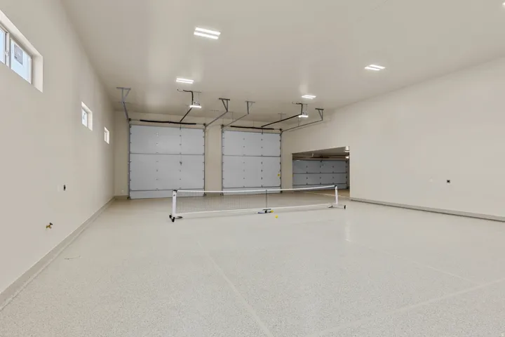 Spacious multi-car garage featuring a light-colored epoxy floor coating, multiple overhead garage doors, recessed ceiling lighting, and high ceilings