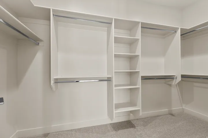 Spacious walk-in closet featuring built-in shelving, multiple hanging rods, and light-toned walls