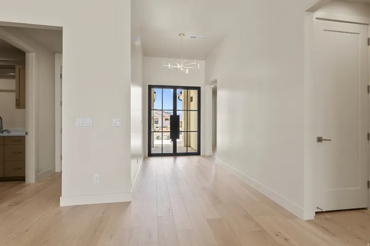 Entryway featuring a black-framed double door with glass panels, light wood-finish flooring, a modern linear chandelier, and high ceilings