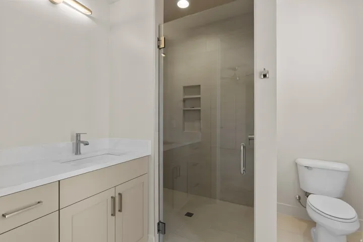 Bathroom featuring a glass-enclosed shower with integrated shelving, a single vanity with an undermount sink, a white countertop, and a contemporary wall-mounted light fixture