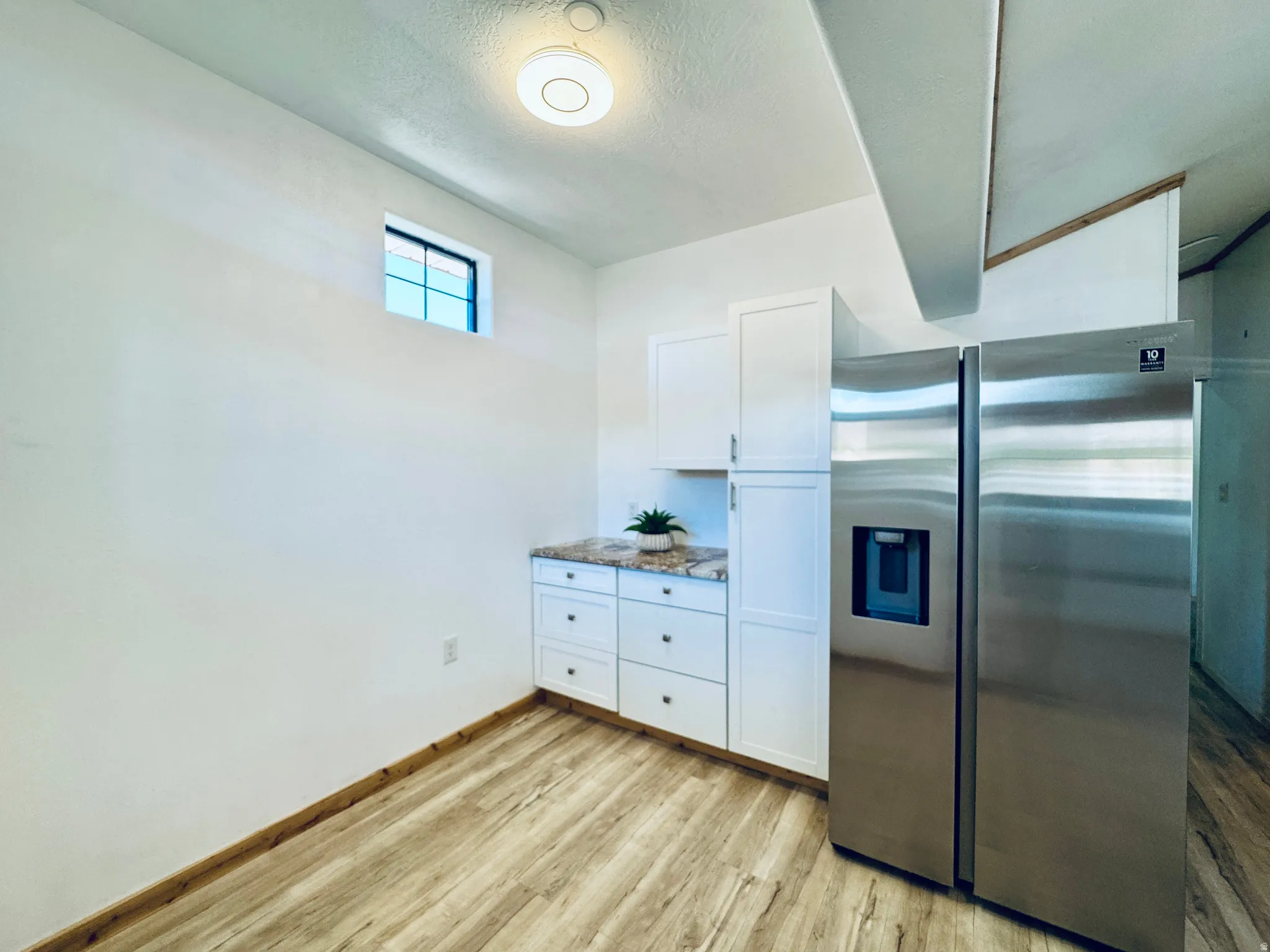 Stainless steel side-by-side refrigerator, white cabinetry, speckled countertop, and wood-finish flooring