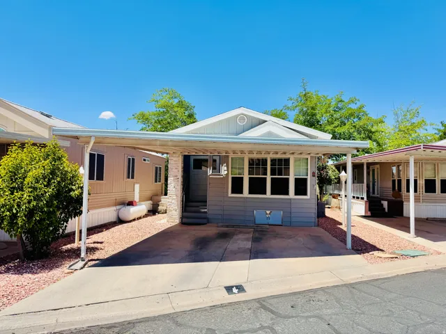Residential property featuring a light grey exterior with white trim, a covered carport, and a stone accent entryway