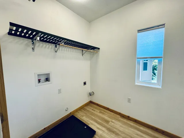 Utility room featuring wood-finish flooring, a wall-mounted shelving unit with a hanging rod, and a window with a cellular shade