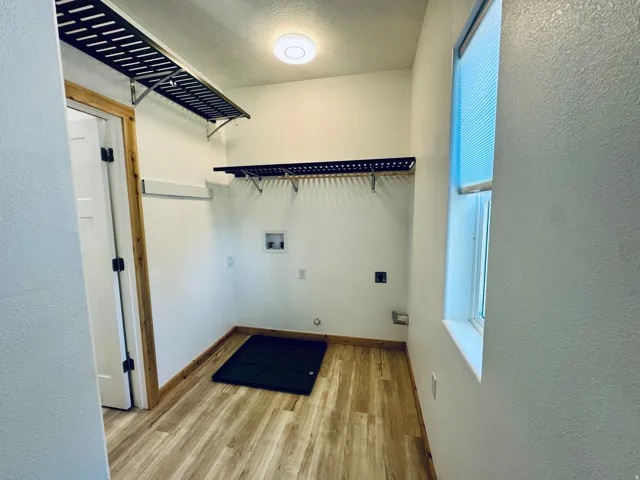 Laundry area featuring wood-finish flooring, two upper wire shelving units, and a window with blinds