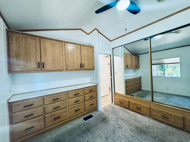 Built-in wood-finish cabinetry and dresser drawers, mirrored sliding closet doors, vaulted ceiling, and ceiling fan