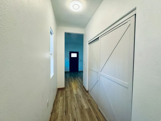 Hallway featuring wood-finish flooring, a flush-mount ceiling light, a window, and white sliding barn-style doors