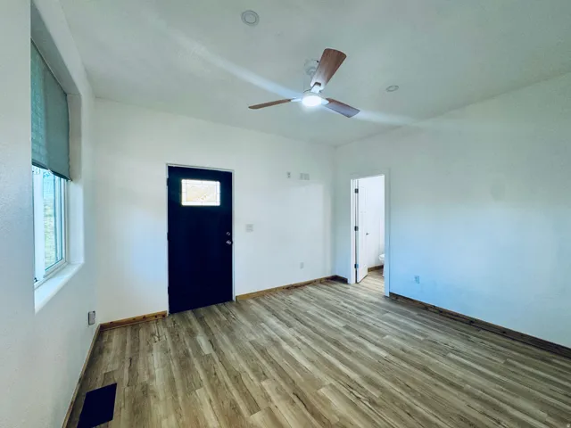 Spacious room featuring wood-finish flooring, a contemporary ceiling fan with integrated lighting, recessed ceiling lights, and a window with a roller shade