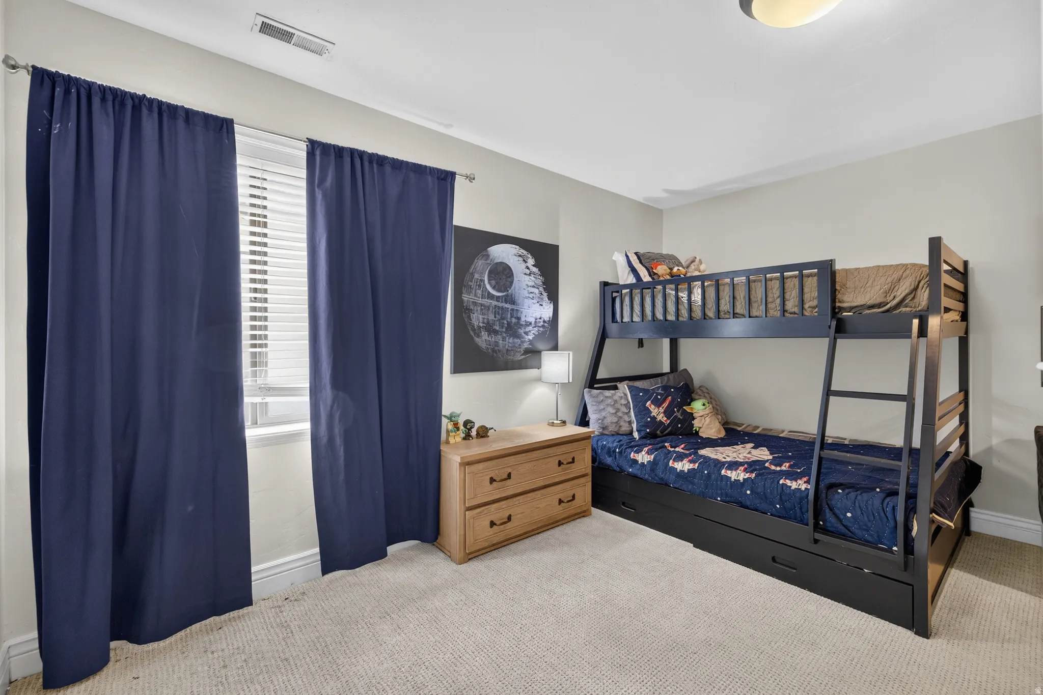 Carpeted room featuring a window with horizontal blinds and full-length blue drapes, a bunk bed with an integrated ladder, and a flush-mount ceiling light fixture