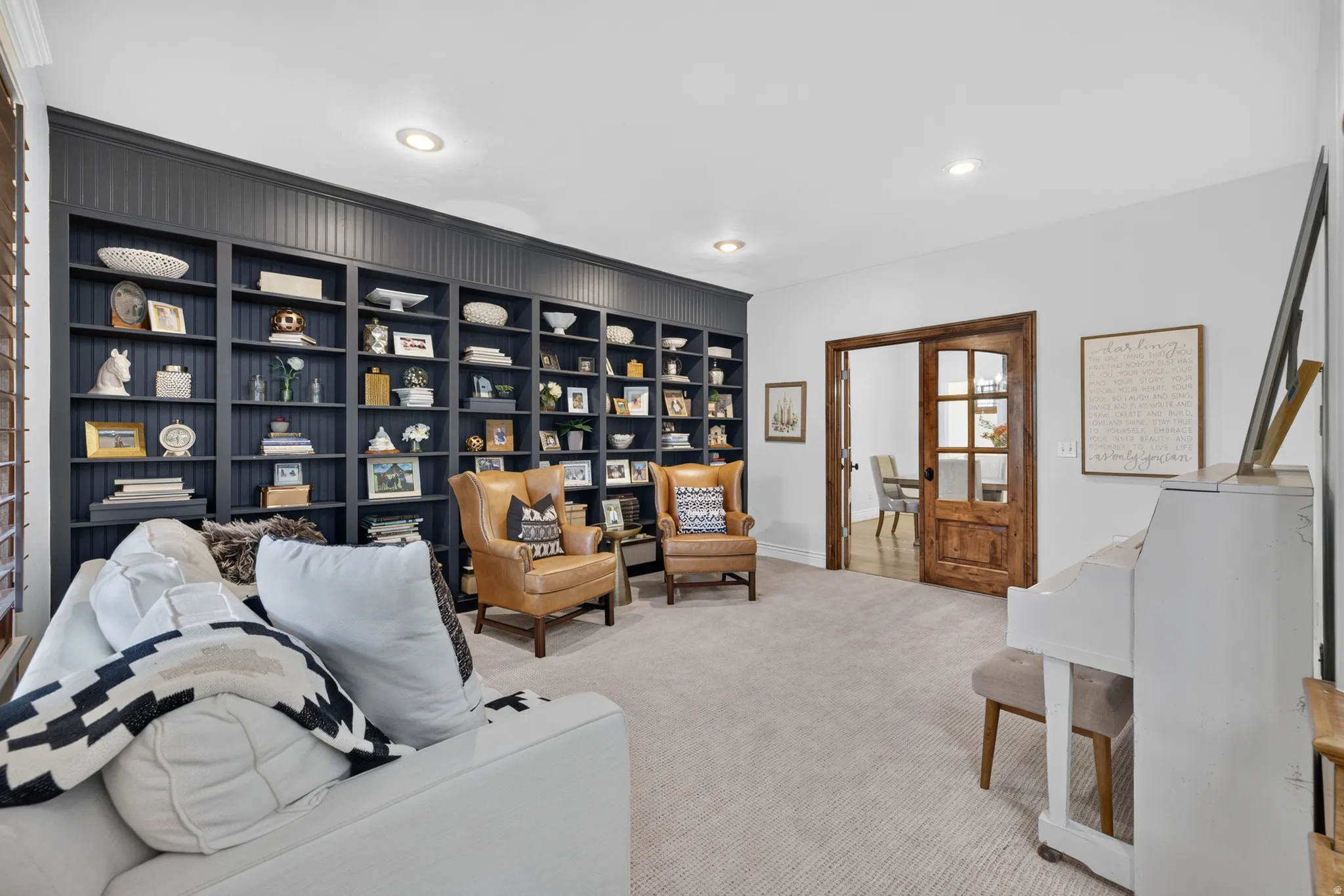Spacious room featuring a full wall of built-in shelving with beadboard detailing, recessed lighting, and light-toned carpeting