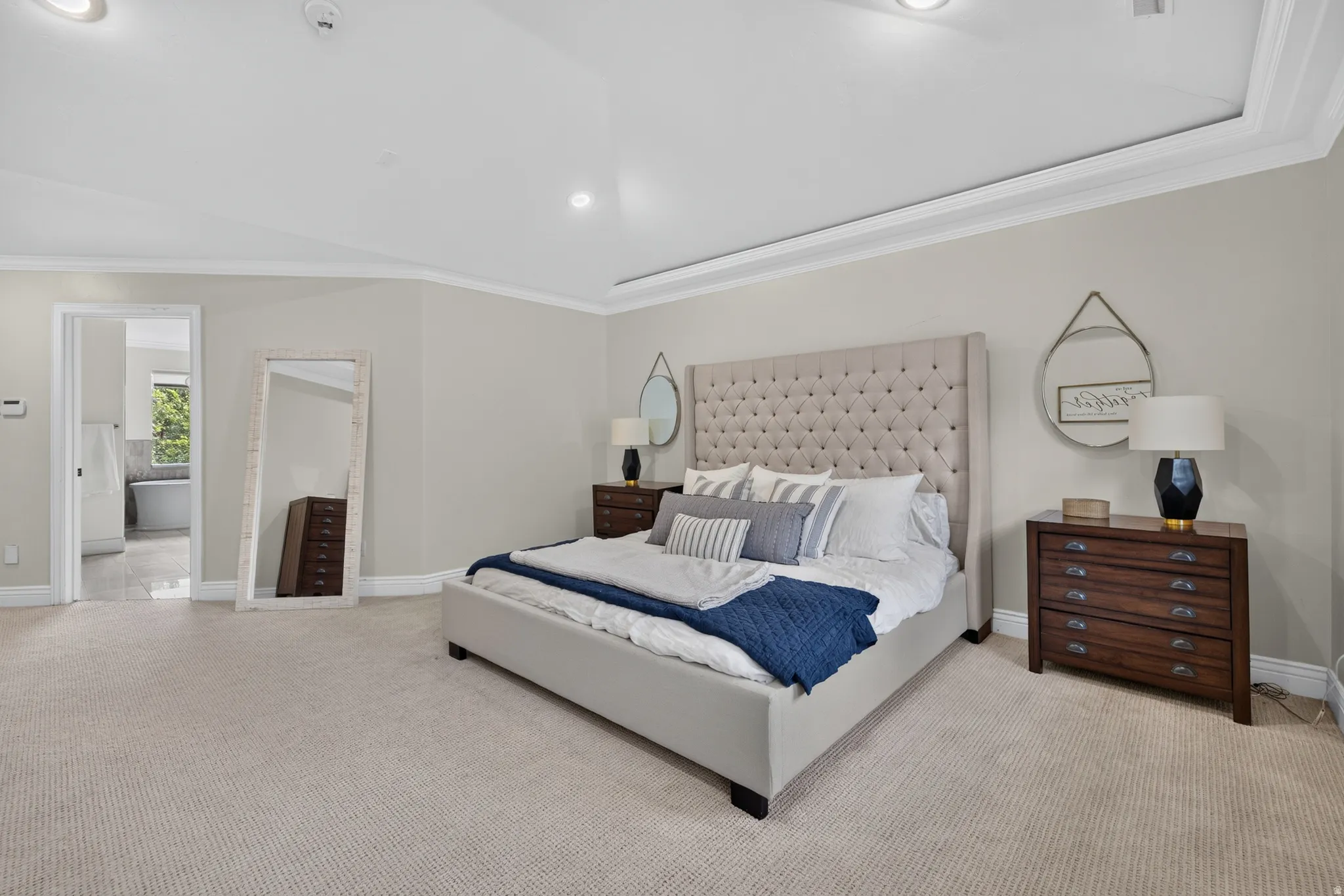 Spacious bedroom featuring neutral carpeting, tray ceiling with recessed lighting, and crown molding