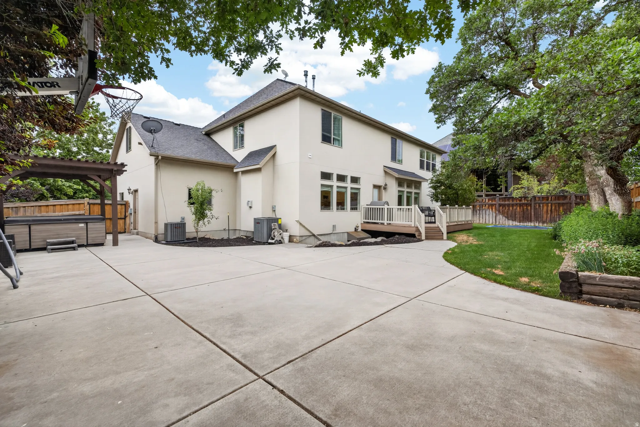 Rear exterior featuring a spacious concrete patio, a multi-level deck with white railings, and a hot tub beneath a wooden pergola