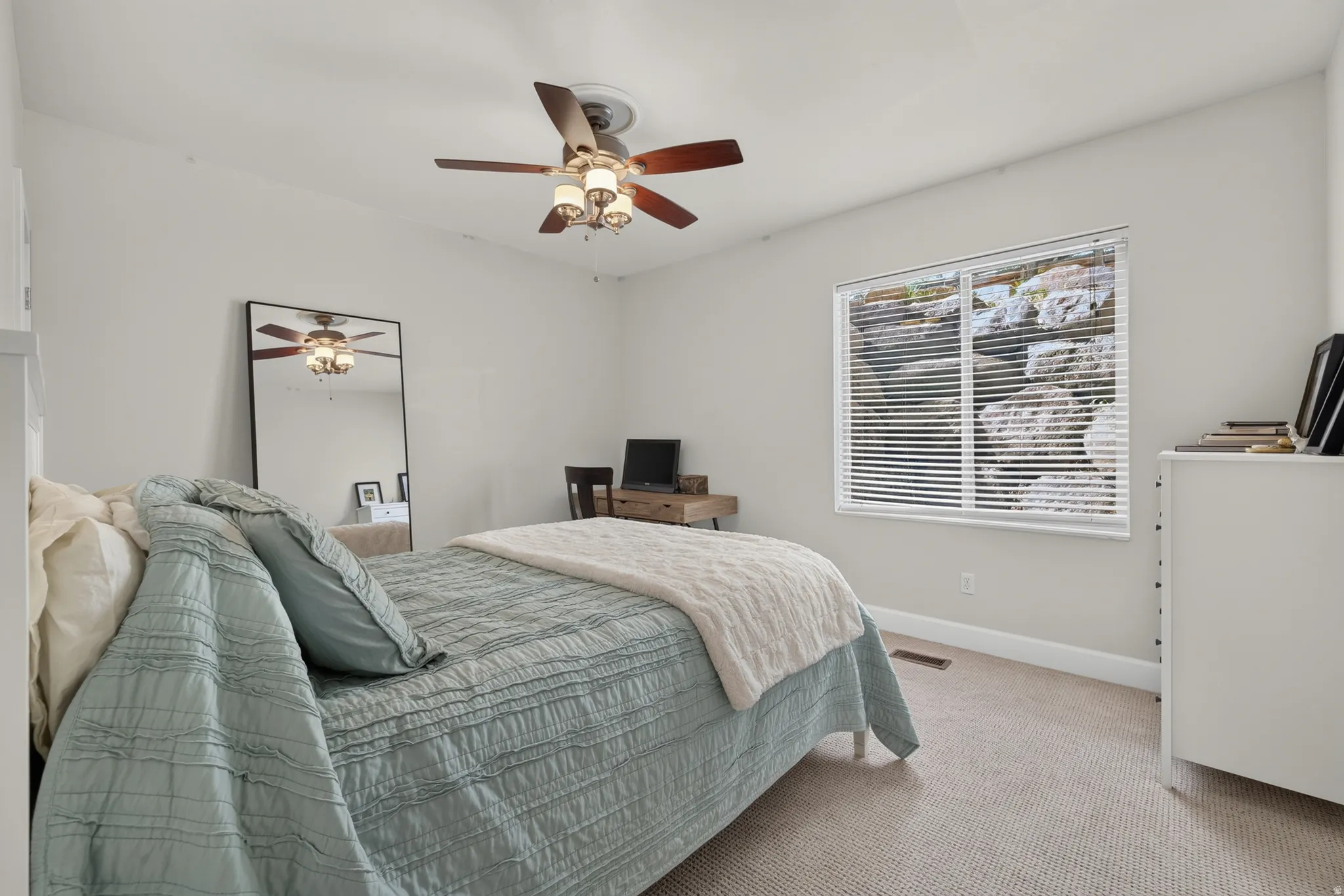 Neutral-toned bedroom featuring a ceiling fan with integrated lighting, a window with horizontal blinds, and light-colored carpeting