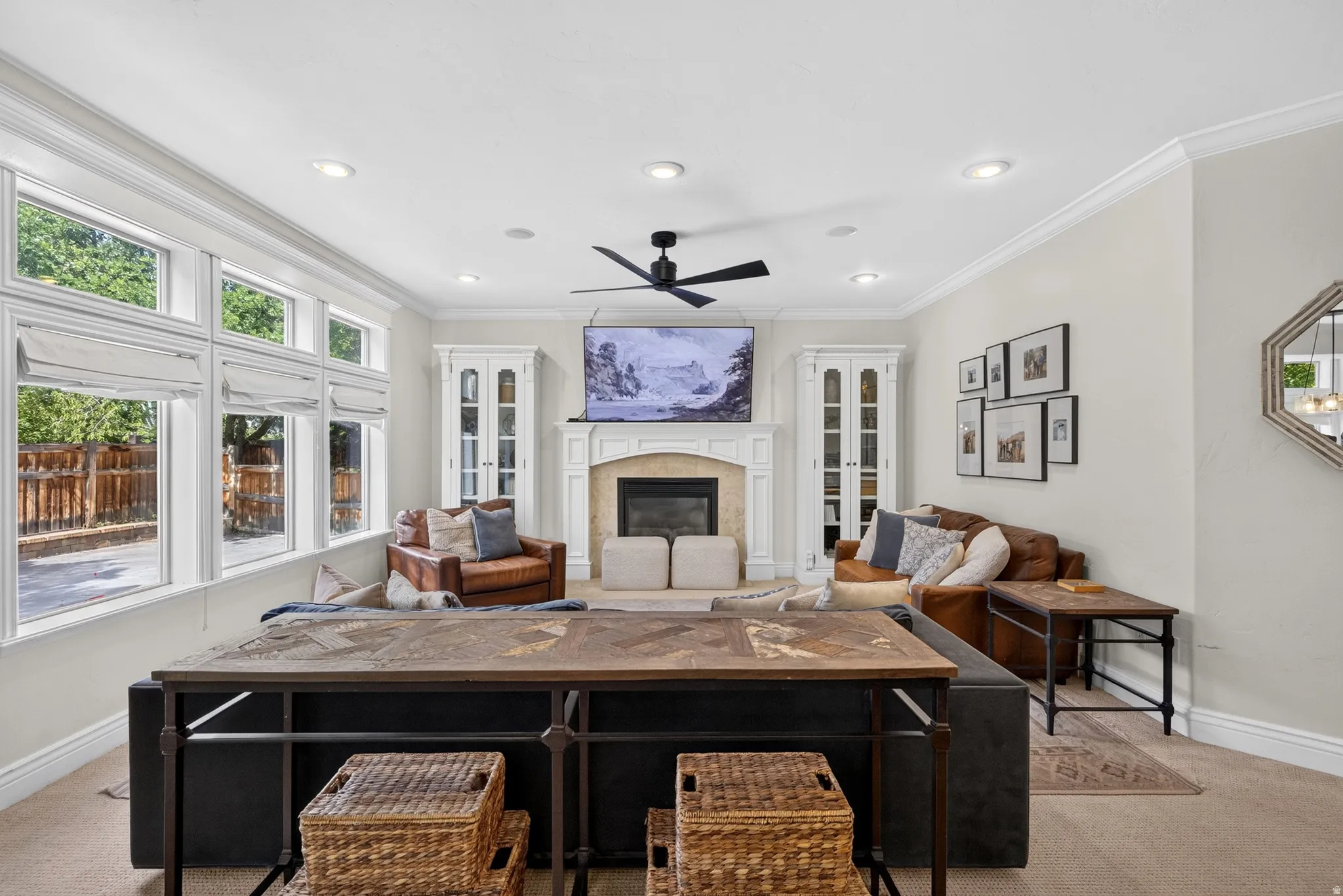 Spacious living area featuring a fireplace with a stone surround and mantel, built-in cabinetry, crown molding, recessed lighting, and a multi-pane window wall