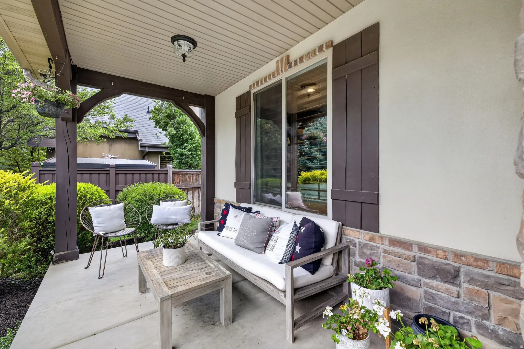 Covered concrete porch featuring a wood-beam archway, stone veneer siding, and a stucco exterior with decorative shutters