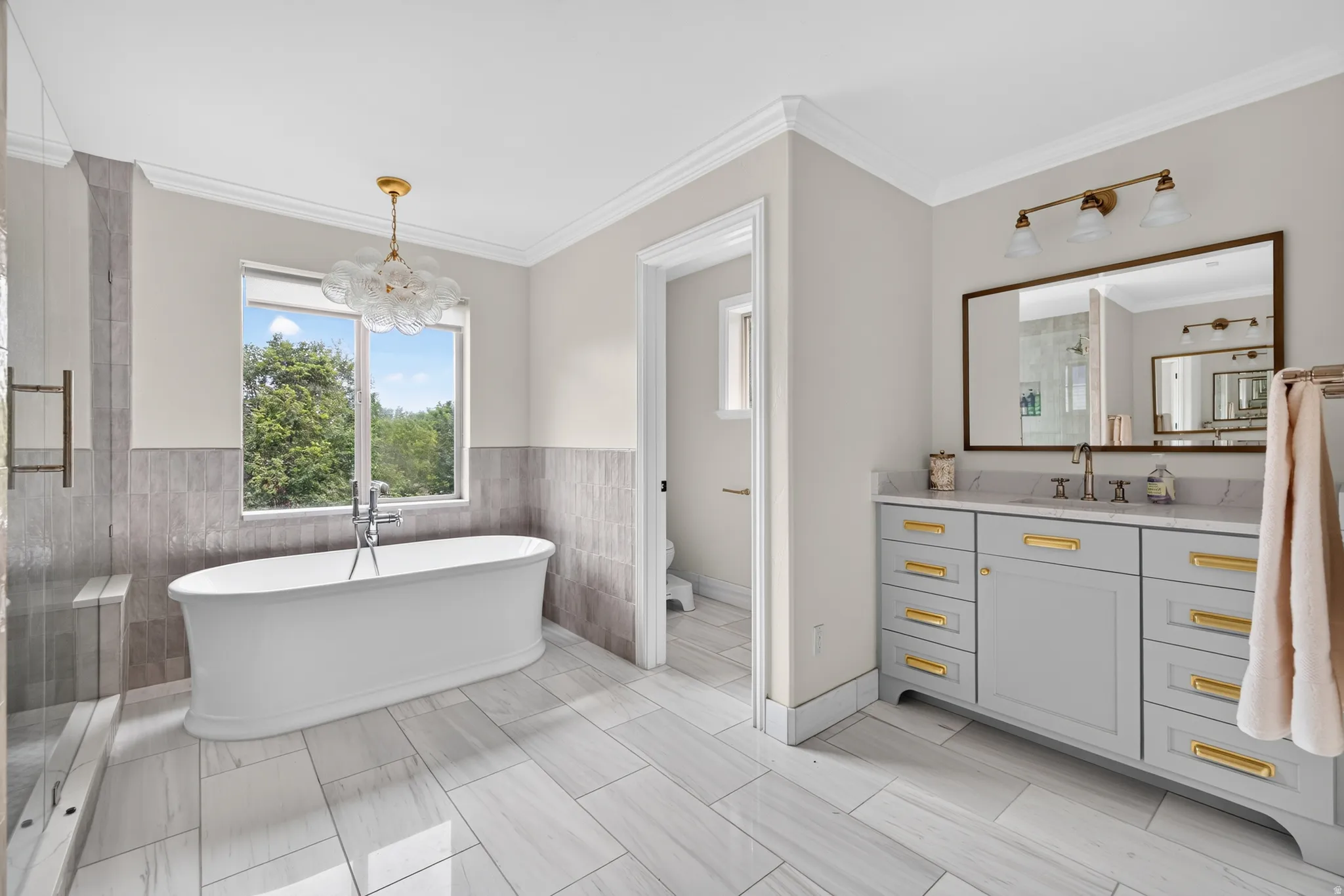 Freestanding soaking tub with a contemporary light fixture, large window, and tile wainscoting