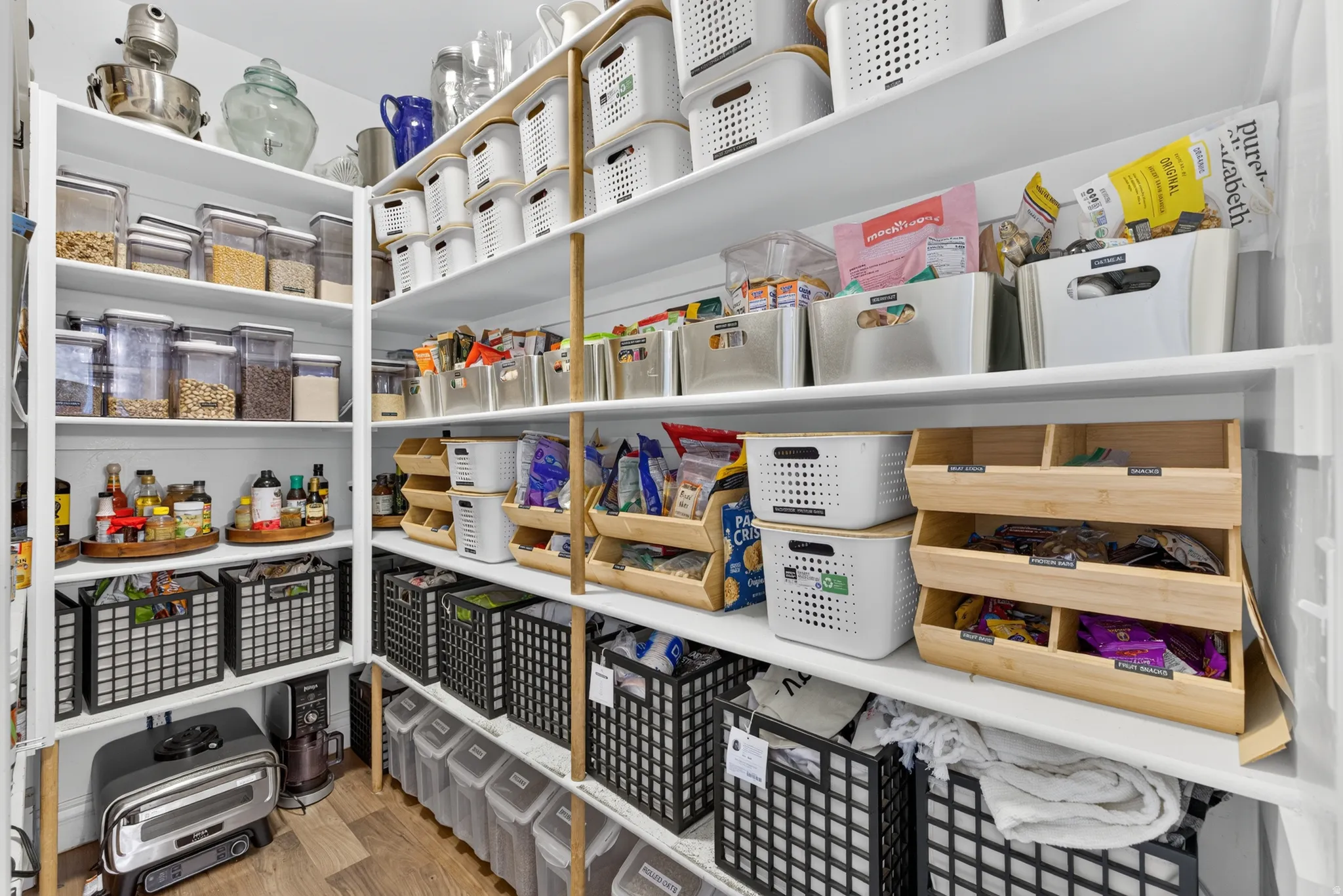 Custom pantry storage system with floor-to-ceiling shelving, wood-finish flooring, and white painted walls