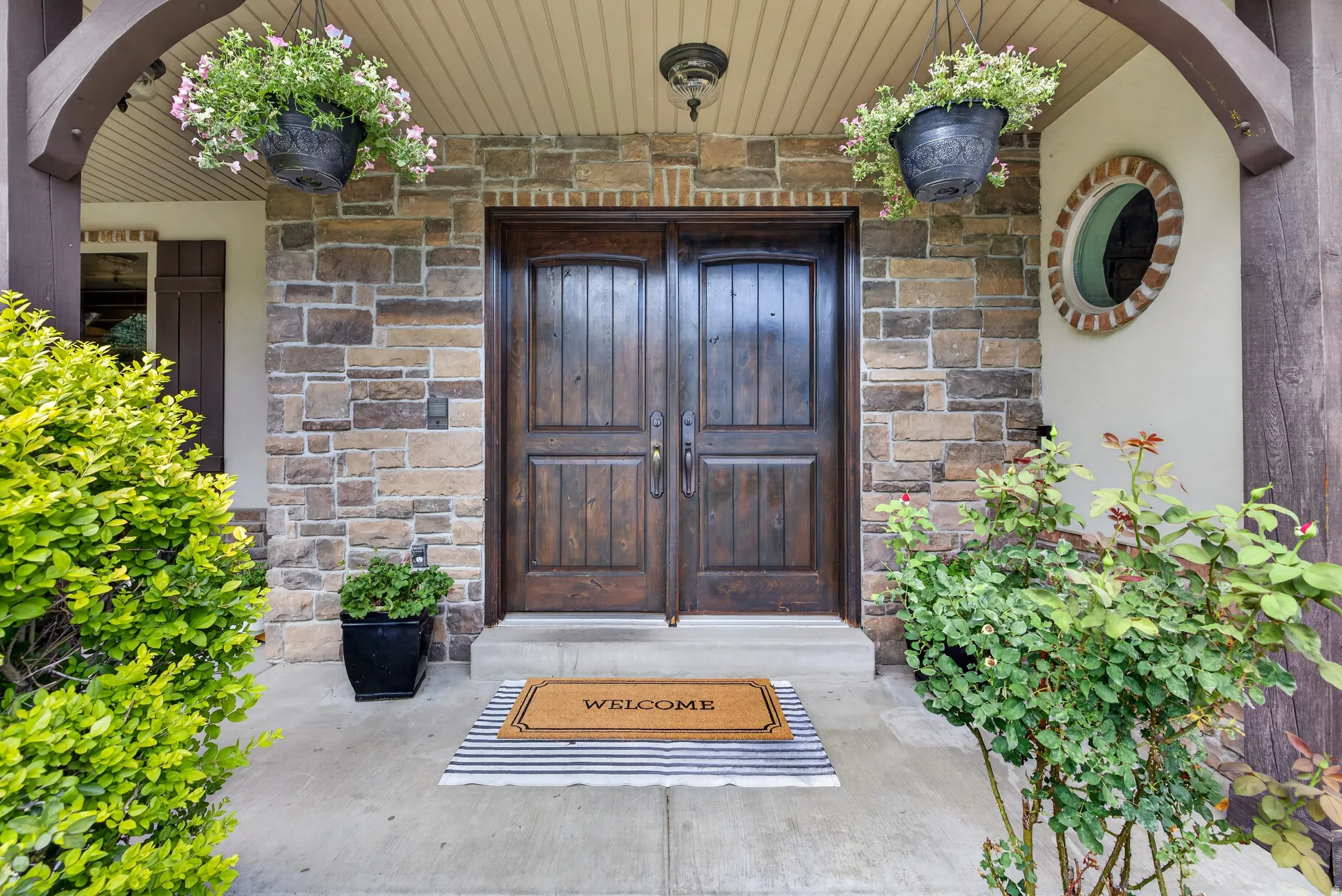 Stone facade entry featuring double wooden doors, a circular window with brick trim, and a covered porch with a beadboard ceiling