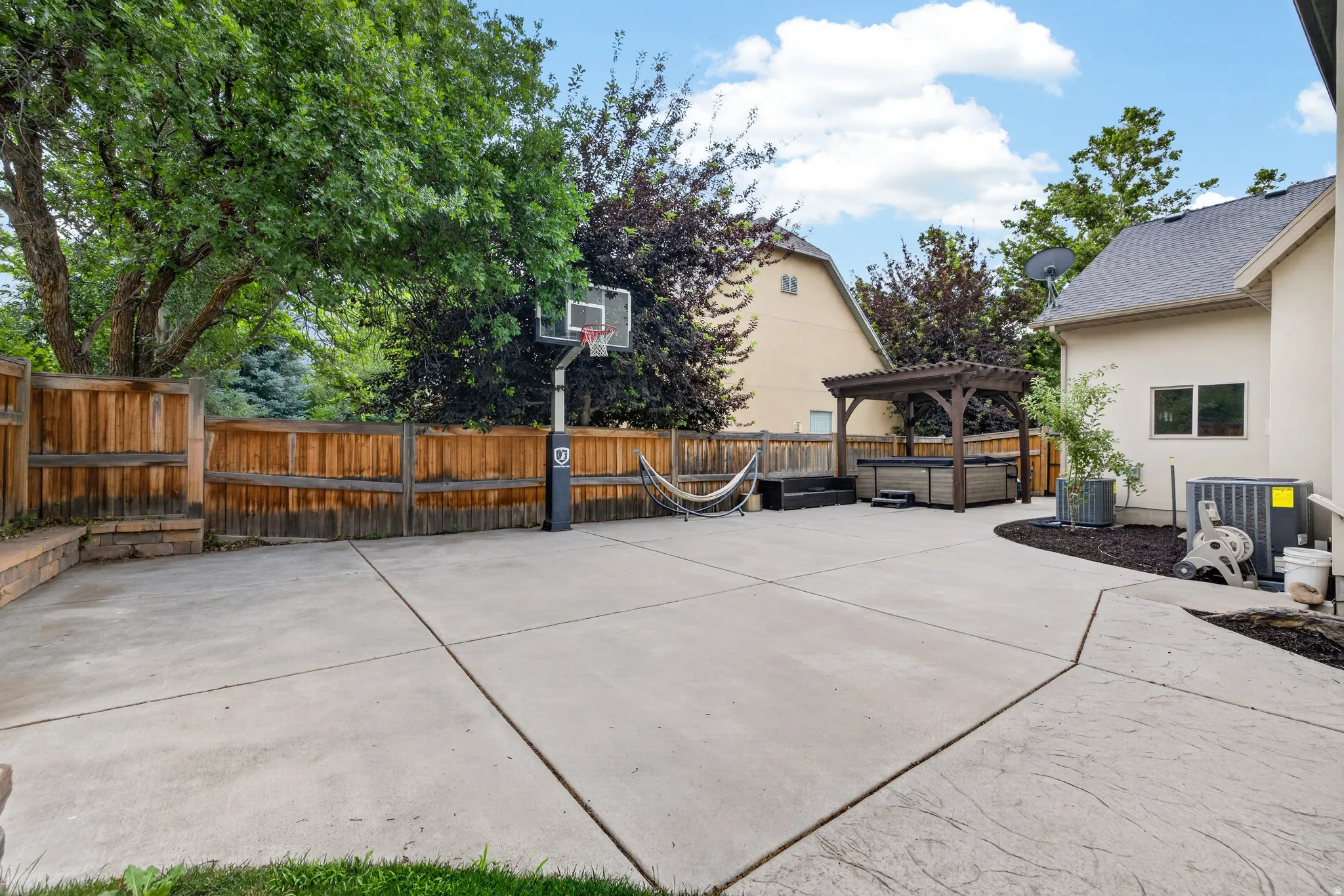 Expansive concrete patio area with a pergola-covered hot tub