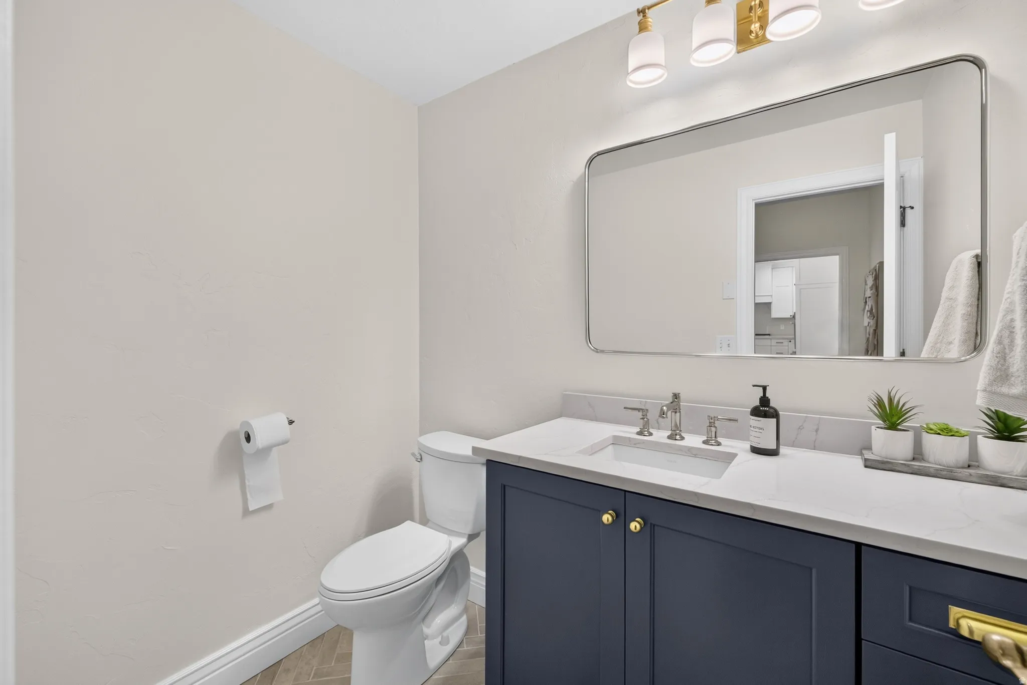Bathroom vanity featuring a quartz countertop with an undermount sink, brass hardware, and a dark blue cabinet