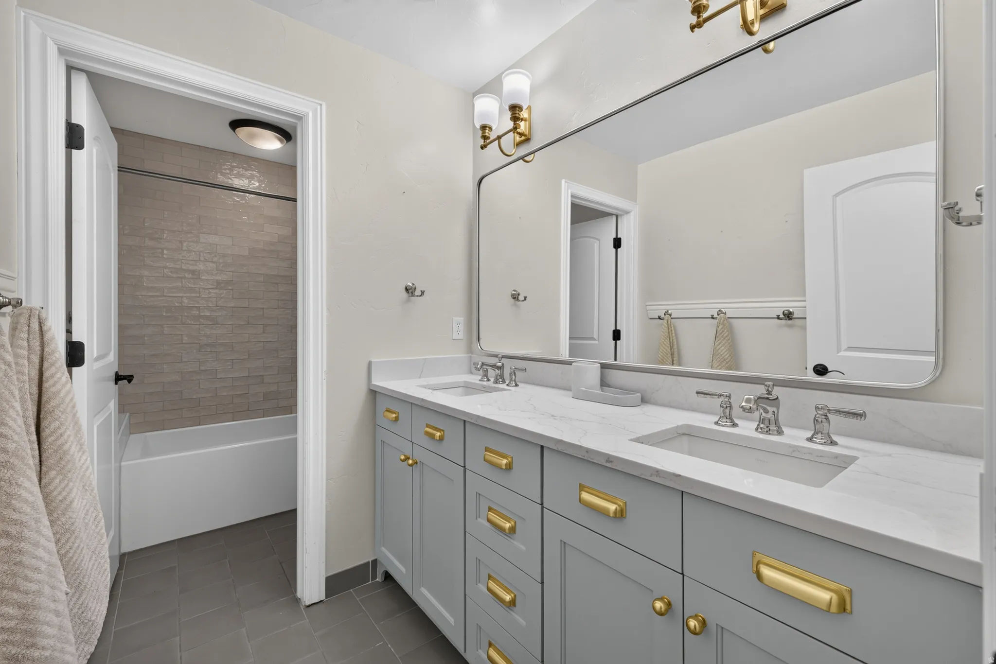 Double vanity featuring light gray cabinetry, gold-tone hardware, and an integrated marble-finish countertop with two undermount sinks