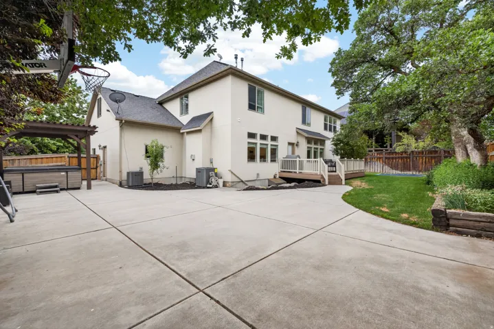 Rear exterior featuring a spacious concrete patio, a multi-level deck with white railings, and a hot tub beneath a wooden pergola