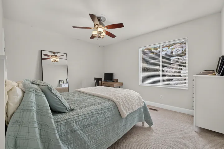 Neutral-toned bedroom featuring a ceiling fan with integrated lighting, a window with horizontal blinds, and light-colored carpeting