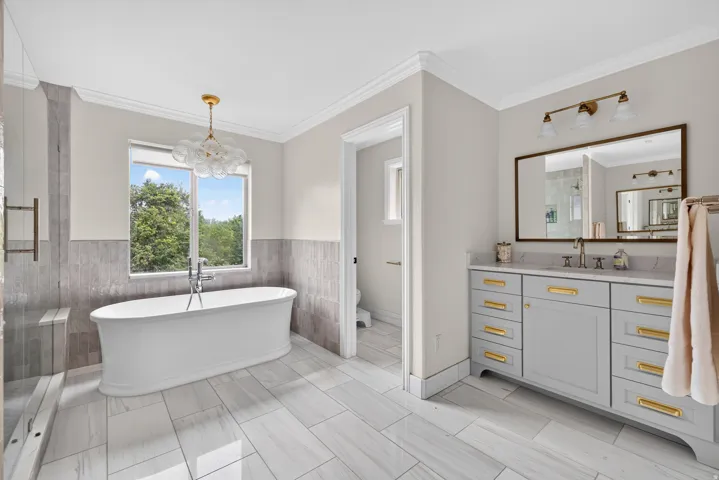 Freestanding soaking tub with a contemporary light fixture, large window, and tile wainscoting
