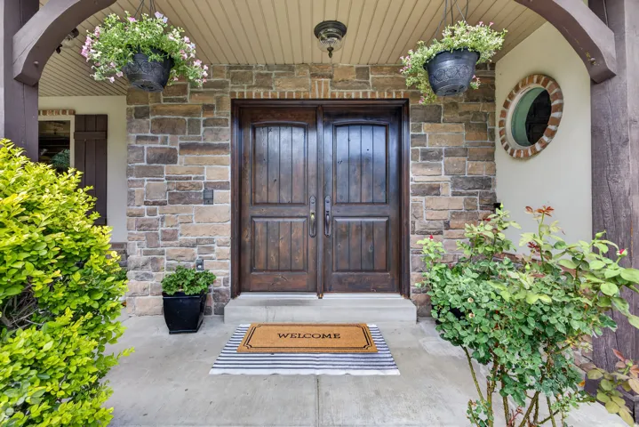 Stone facade entry featuring double wooden doors, a circular window with brick trim, and a covered porch with a beadboard ceiling