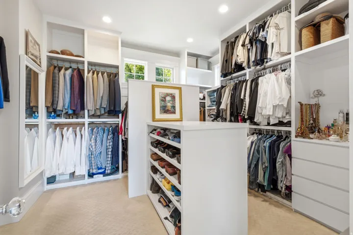 Custom closet system featuring extensive hanging rods, multiple shelving units, built-in drawers, and a central island with integrated shoe storage
