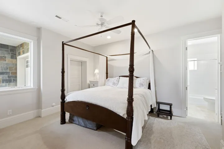 Carpeted bedroom featuring white walls, a ceiling fan, and a wide window with stone wall detailing