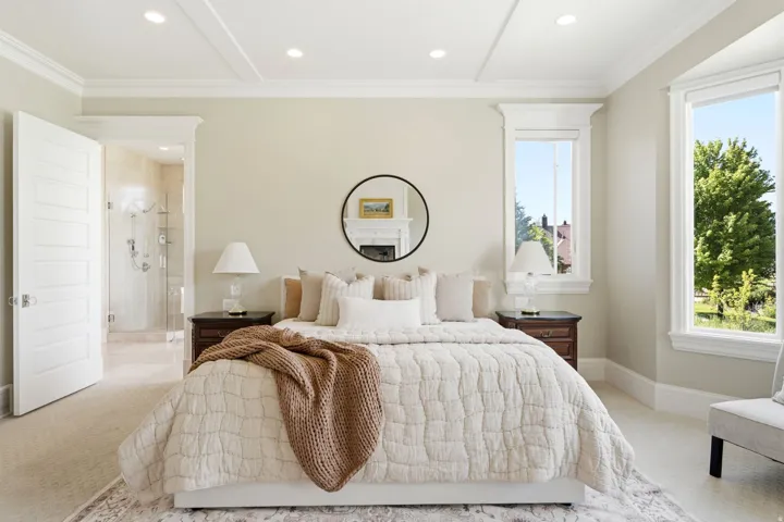 Recessed ceiling lighting with tray ceiling detail, large windows with white trim, and a clear glass shower enclosure