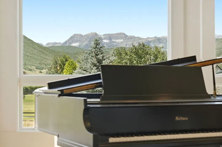 Floor-to-ceiling windows frame a mountain backdrop and lush green landscape