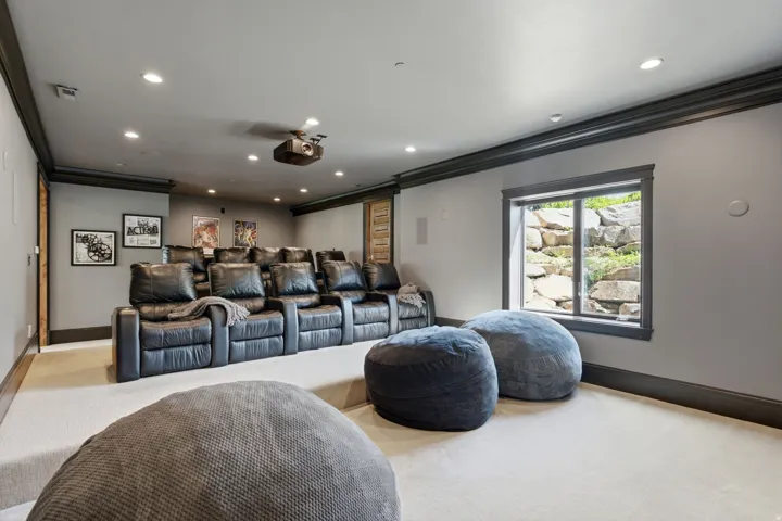 Dedicated home theater featuring tiered seating, recessed lighting, ceiling-mounted projector, and a visible window with rock landscaping outside