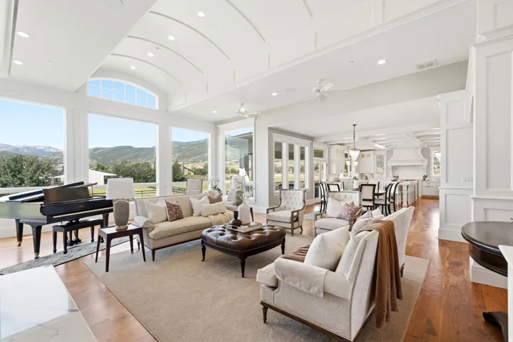 Spacious living area featuring expansive windows, natural wood flooring, a coffered ceiling with recessed lighting, and a neutral color palette