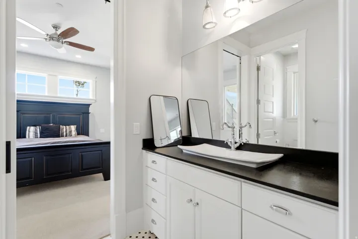 Vanity featuring a white vessel sink, polished chrome faucet, and dark countertop, complemented by white cabinetry with polished chrome hardware
