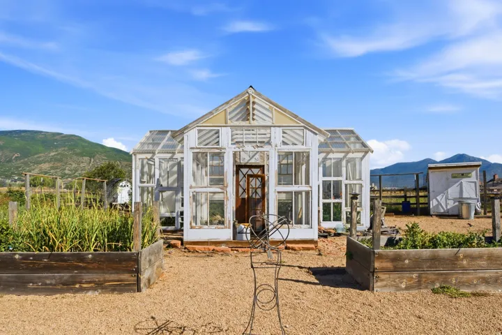 White-framed greenhouse with a wood-panel door, set on a gravel-covered ground