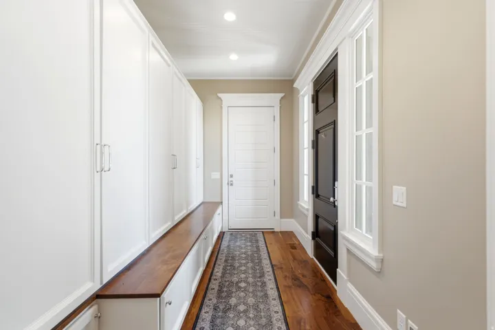 Entryway with wood-finish flooring, a full wall of built-in white cabinetry, and a dark paneled door with sidelight windows