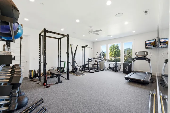 Spacious recreation room featuring light gray carpet flooring, recessed lighting, a ceiling fan, and large windows with mountain and tree scenery