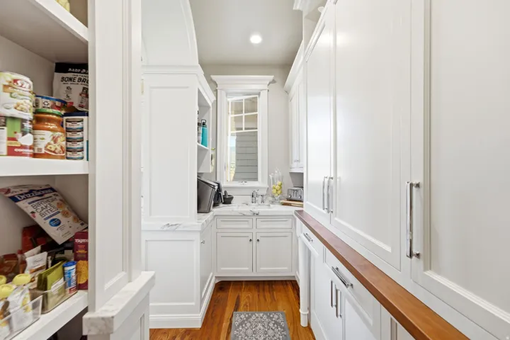 Walk-in pantry with extensive built-in shelving, white cabinetry, a built-in sink, and wood-finish flooring