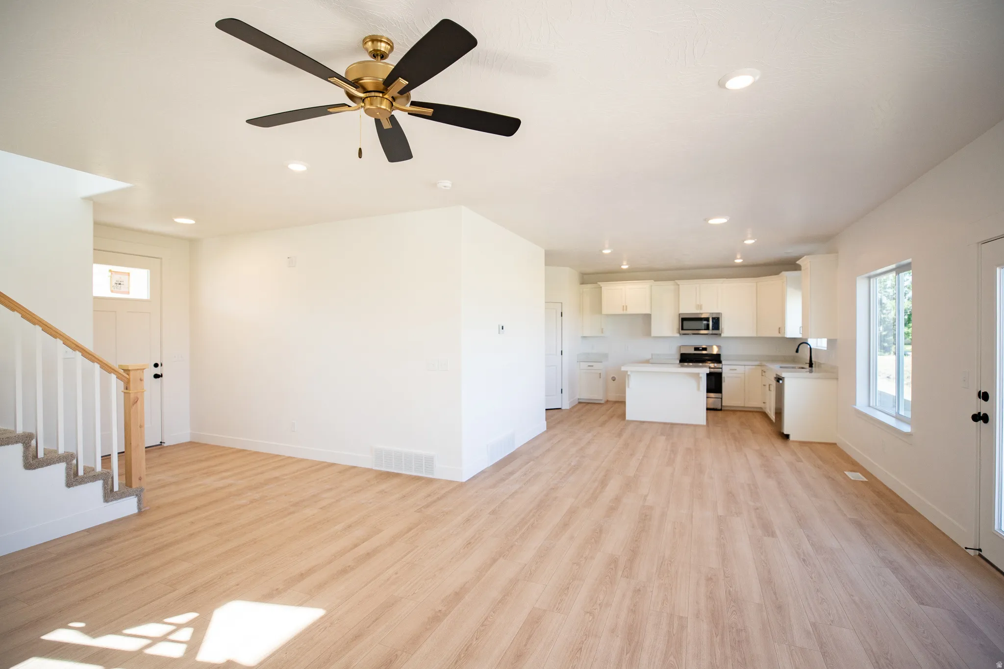 Large, open concept great room with wood laminate flooring, a ceiling fan, recessed lighting, and an upgraded staircase