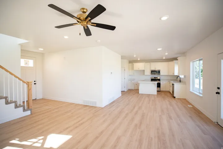 Large, open concept great room with wood laminate flooring, a ceiling fan, recessed lighting, and an upgraded staircase