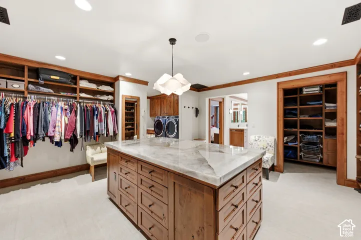 Central wood-finish island with stone countertop, built-in shelving, integrated laundry appliances, and recessed lighting